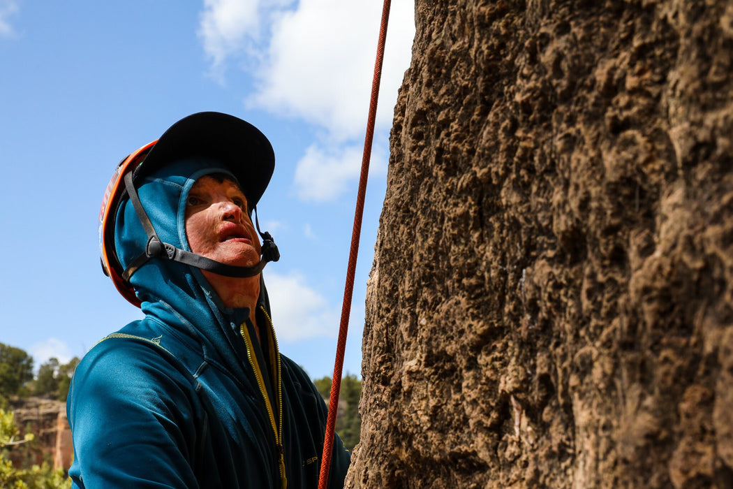 Person climbing a rock face with a helmet and blue jacket.