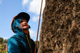 Person climbing a rock face with a helmet and blue jacket.