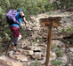 Hiker with a prosthetic leg on a rocky trail next to a signpost with 'The Piggy Bank' written on it.
