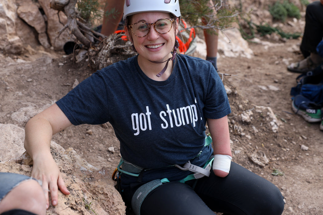Person wearing a 'got stump?' shirt sitting on a rock outdoors