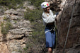 Person rock climbing with a helmet and safety harness in a natural rocky landscape