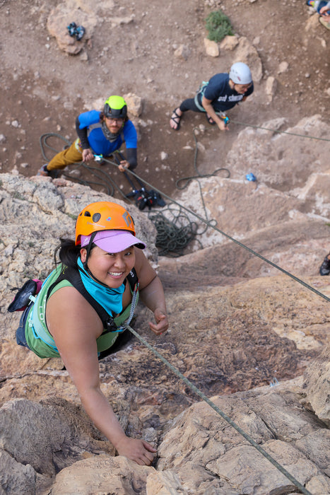 Person climbing a rocky mountain with others in the background.