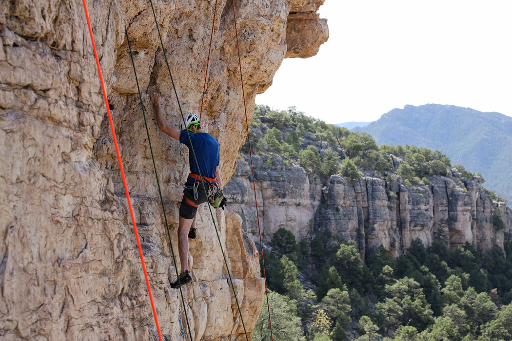 Person climbing a rocky cliff with a scenic mountain background