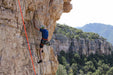 Person climbing a rocky cliff with a scenic mountain background