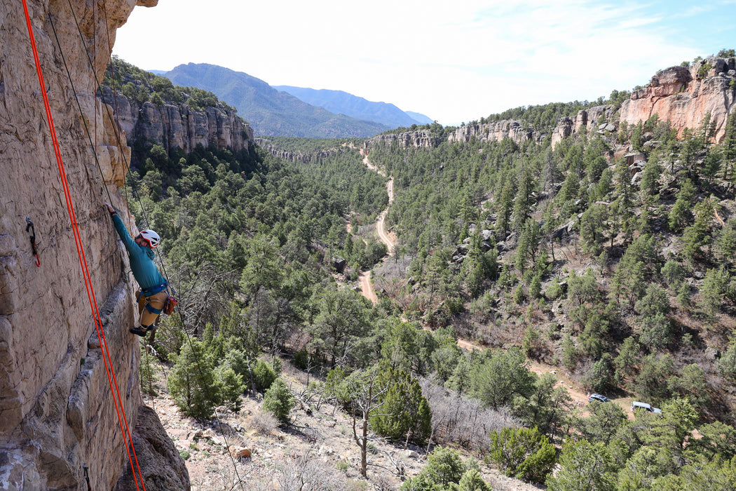 Person rock climbing on a cliff with a scenic view of a valley and mountains.