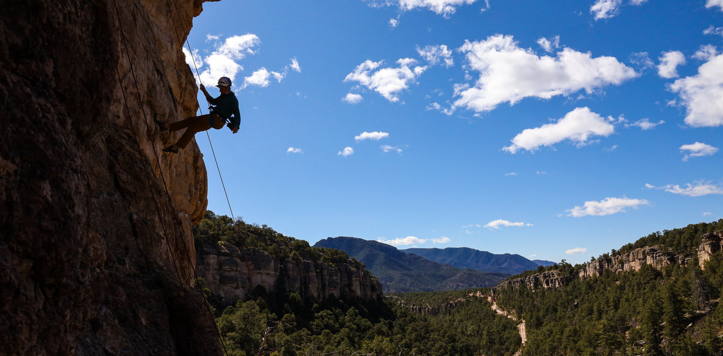 Person climbing a rocky cliff with a scenic landscape in the background
