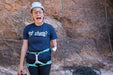 Person in climbing gear with a helmet and harness, standing against a rock wall.