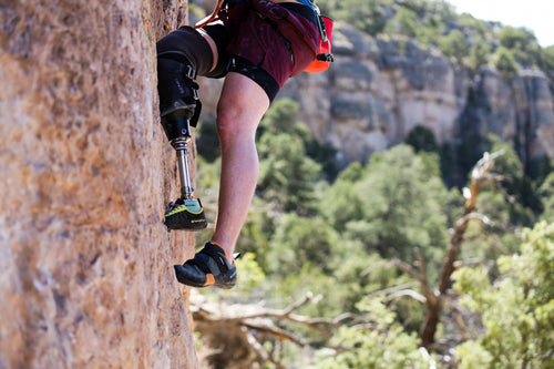Person with a prosthetic climbing a rock face in a natural setting