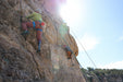 Person rock climbing on a steep cliff with a clear sky above.
