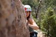 Person climbing a rock face with a helmet on, surrounded by trees.