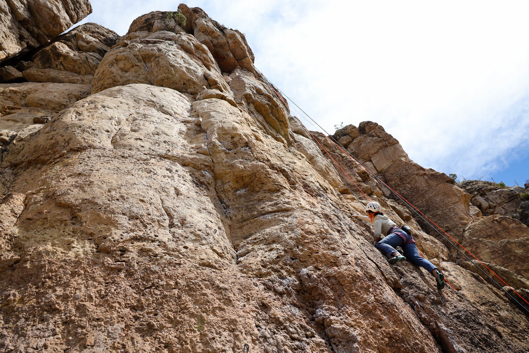 Person climbing a rocky cliff face with a clear sky above