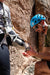 Person climbing a rock wall with another person assisting attaching a prosthetic to the socket, wearing a blue helmet and sunglasses.