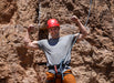 Man in climbing gear flexing muscles against a rock wall