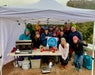 Group of people under a tent with a table displaying a Paradox Sports flag, set against a natural landscape.