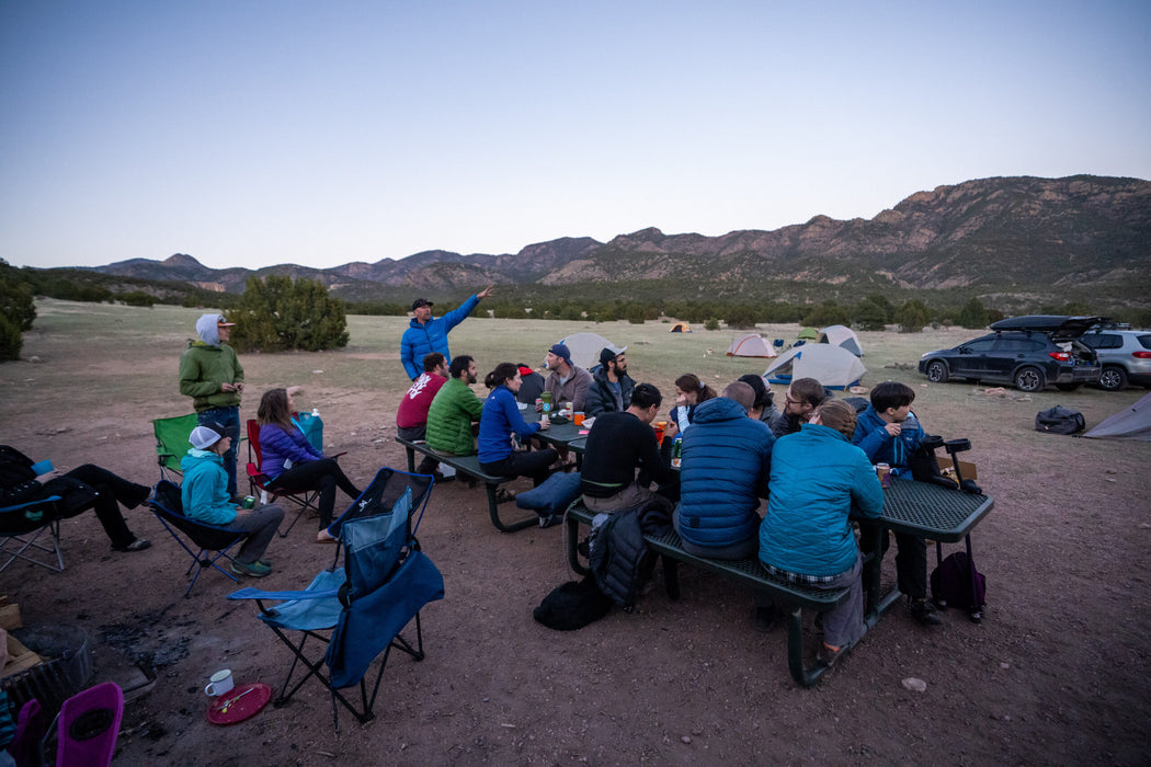 Group of people camping outdoors with mountains in the background.