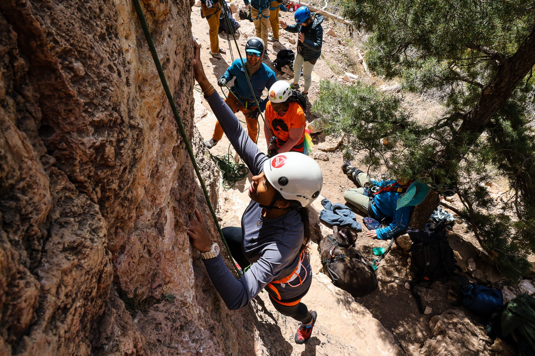 Person climbing a rock face with others in the background