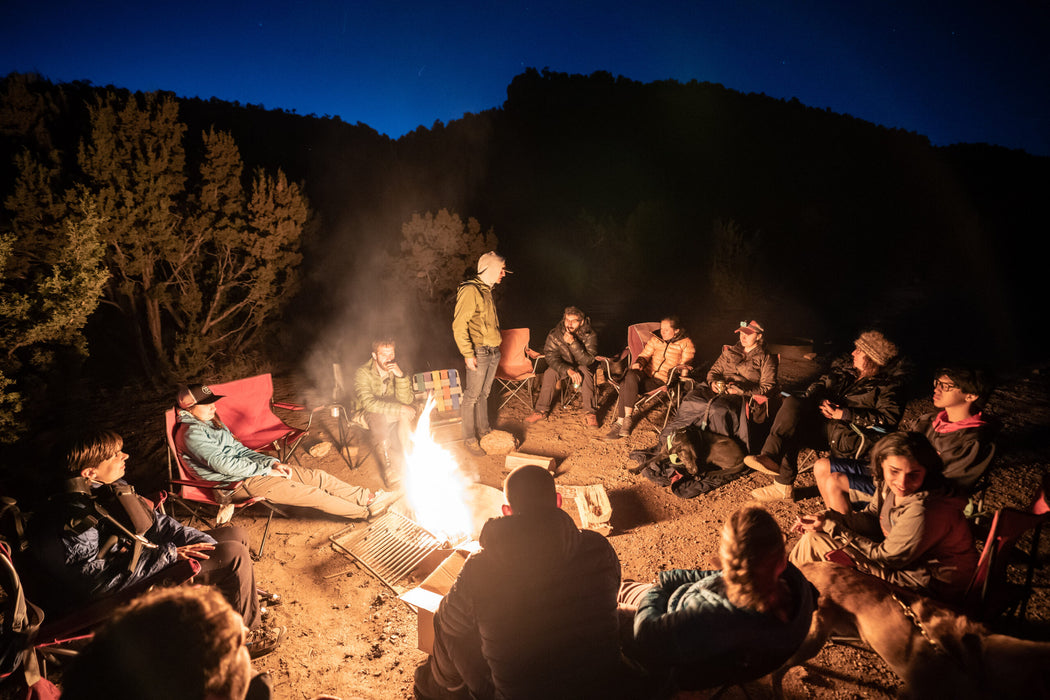 Group of people gathered around a campfire in a mountainous area at night.