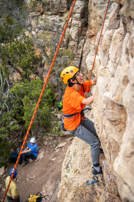 Person climbing a rock face with safety ropes in a natural setting