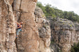 Person climbing a rocky cliff with greenery in the background