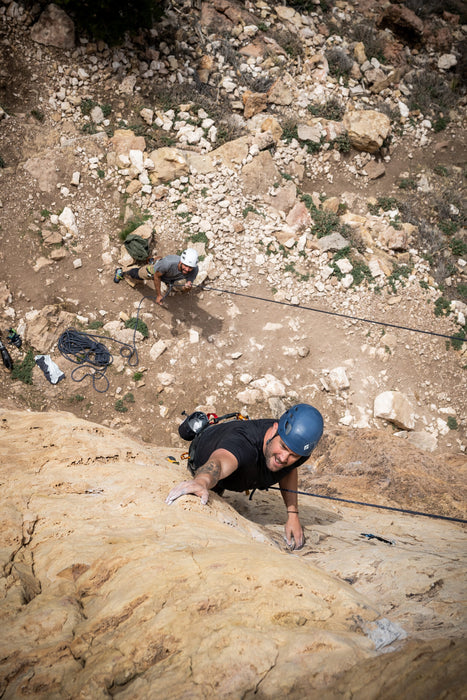 Person climbing a rocky cliff with ropes and equipment on a mountain.