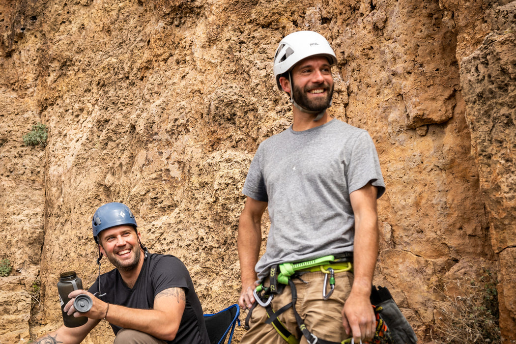 Two climbers with climbing gear standing against a rock wall.