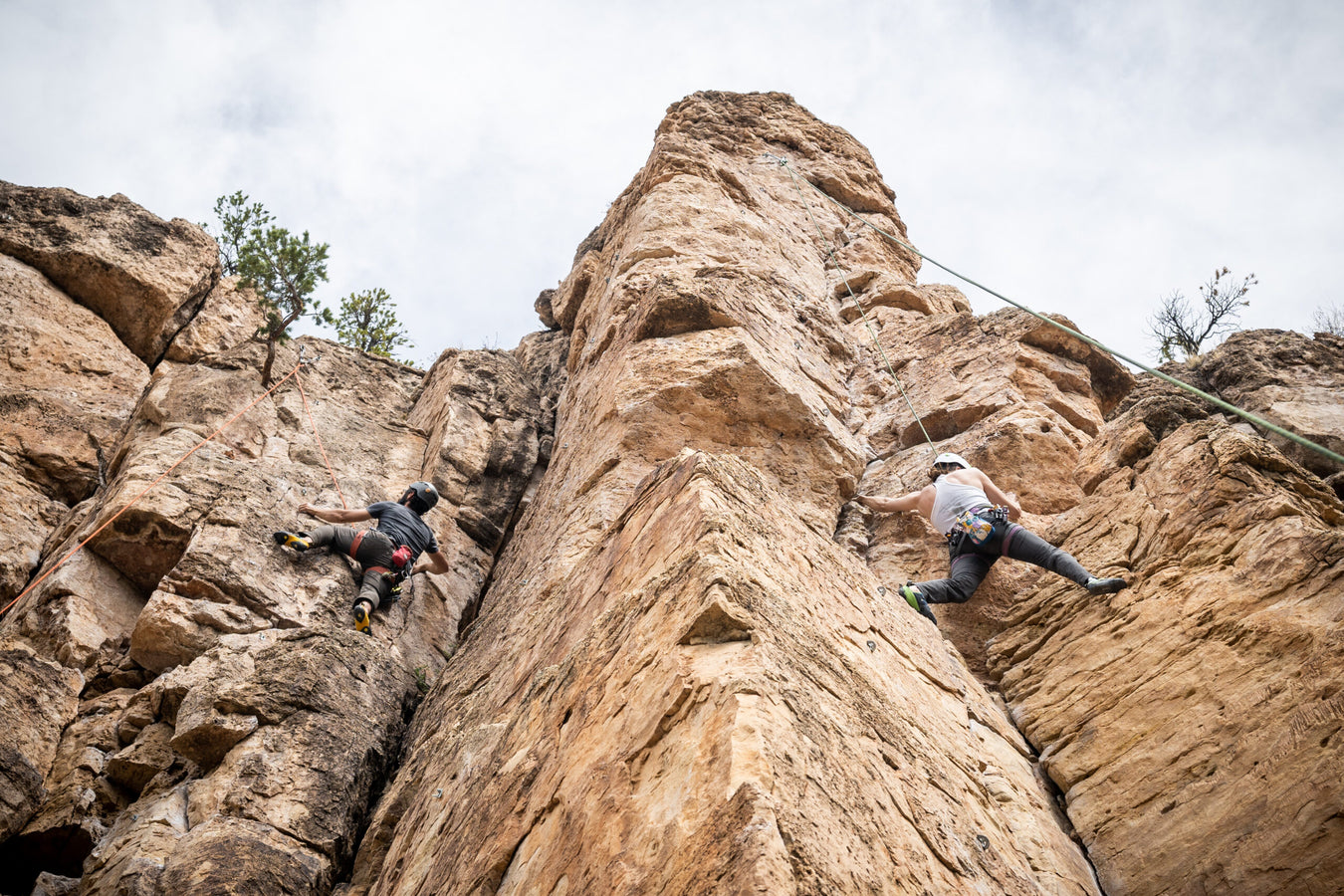 Two climbers on a rocky cliff face with a cloudy sky.