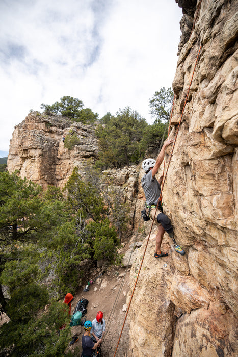 Person rock climbing on a rocky cliff with others below.