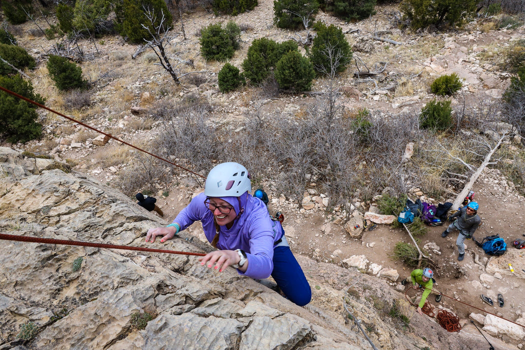 Person rock climbing on a rocky cliff with others in the background
