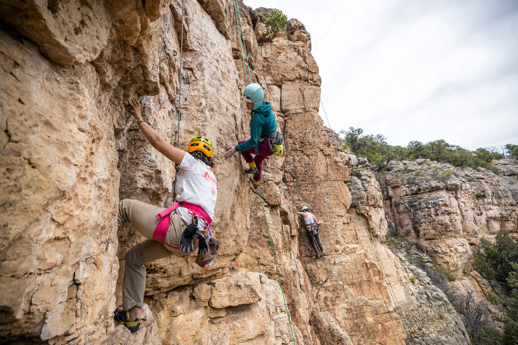 Three climbers on a rocky cliff face with a clear sky.