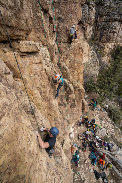 Rock climbers on a steep cliff with spectators below.