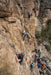 Rock climbers on a steep cliff with spectators below.