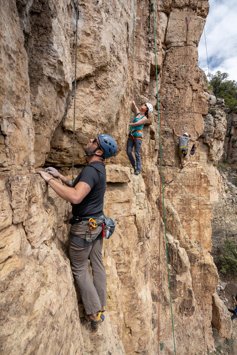 Three climbers on a rocky cliff face with safety ropes.