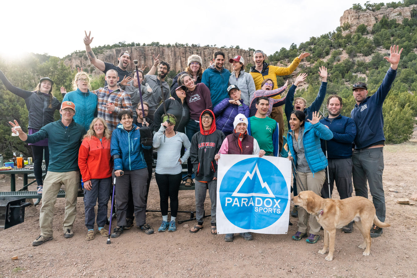 Group of people posing outdoors with a Paradox Sports sign and a dog.