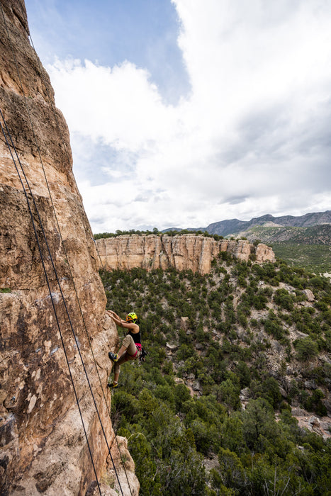 Person rock climbing on a steep cliff with a scenic mountain landscape.
