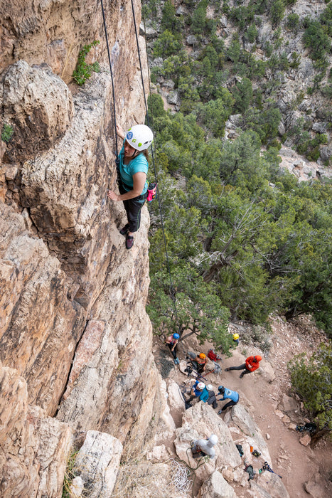 Person climbing a steep cliff with others at the base in a mountainous area