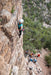 Person climbing a steep cliff with others at the base in a mountainous area