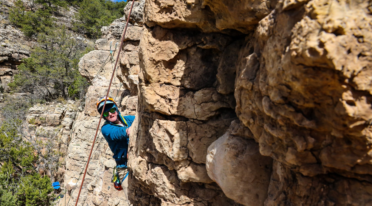 Person rock climbing on a rocky cliff face with ropes and climbing gear.