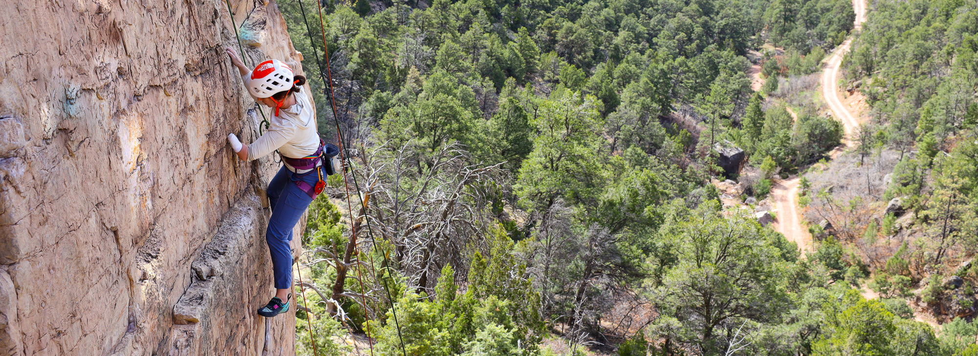 Person with arm amputation climbing a rocky cliff with a scenic background of trees and a trail on Paradox Sports Climbing Trip