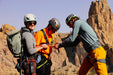 Three climbers preparing for a climb with rocky cliffs in the background.