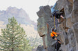 Two climbers on a rocky cliff with mountains in the background.