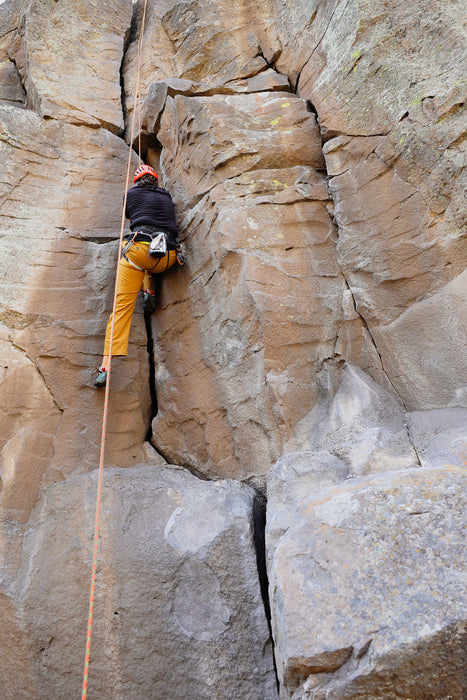 Person climbing a rocky cliff face with a rope.