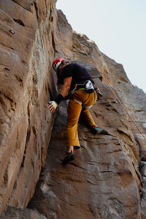 Person climbing a rocky cliff face with safety gear.