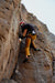 Person climbing a rocky cliff face with safety gear.