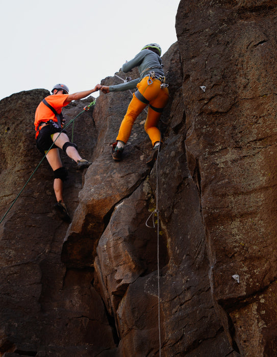 Two climbers on a rocky cliff face fist bumping the other.