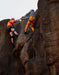 Two climbers on a rocky cliff face fist bumping the other.