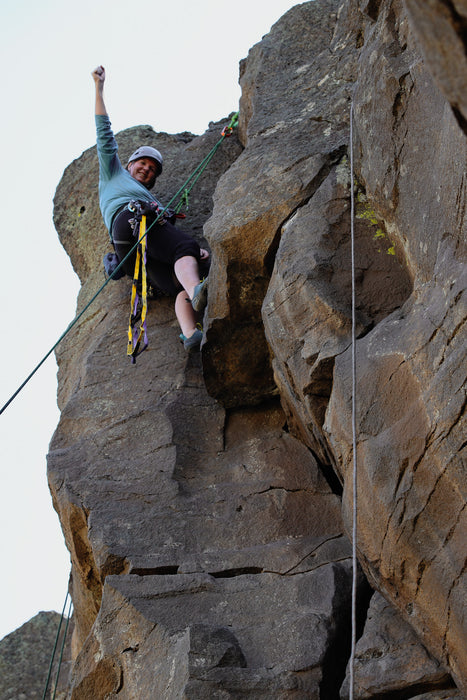 Person climbing a rocky cliff face with ropes and gear.