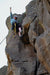 Person climbing a rocky cliff face with ropes and gear.