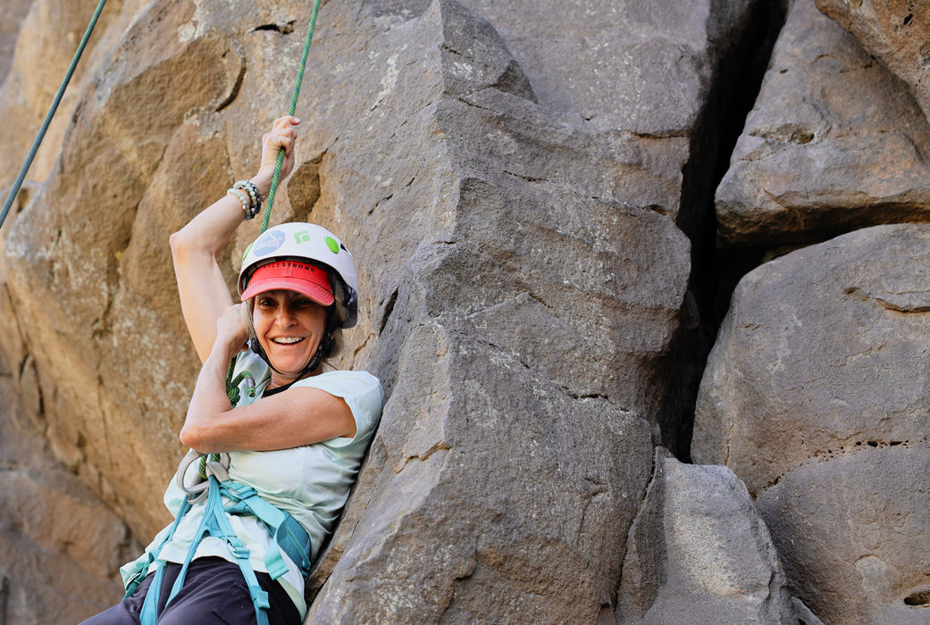 Person climbing a rocky cliff face wearing a helmet and safety harness.