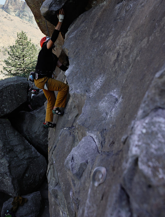 Person climbing a rocky cliff face with mountainous background.