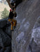Person climbing a rocky cliff face with mountainous background.